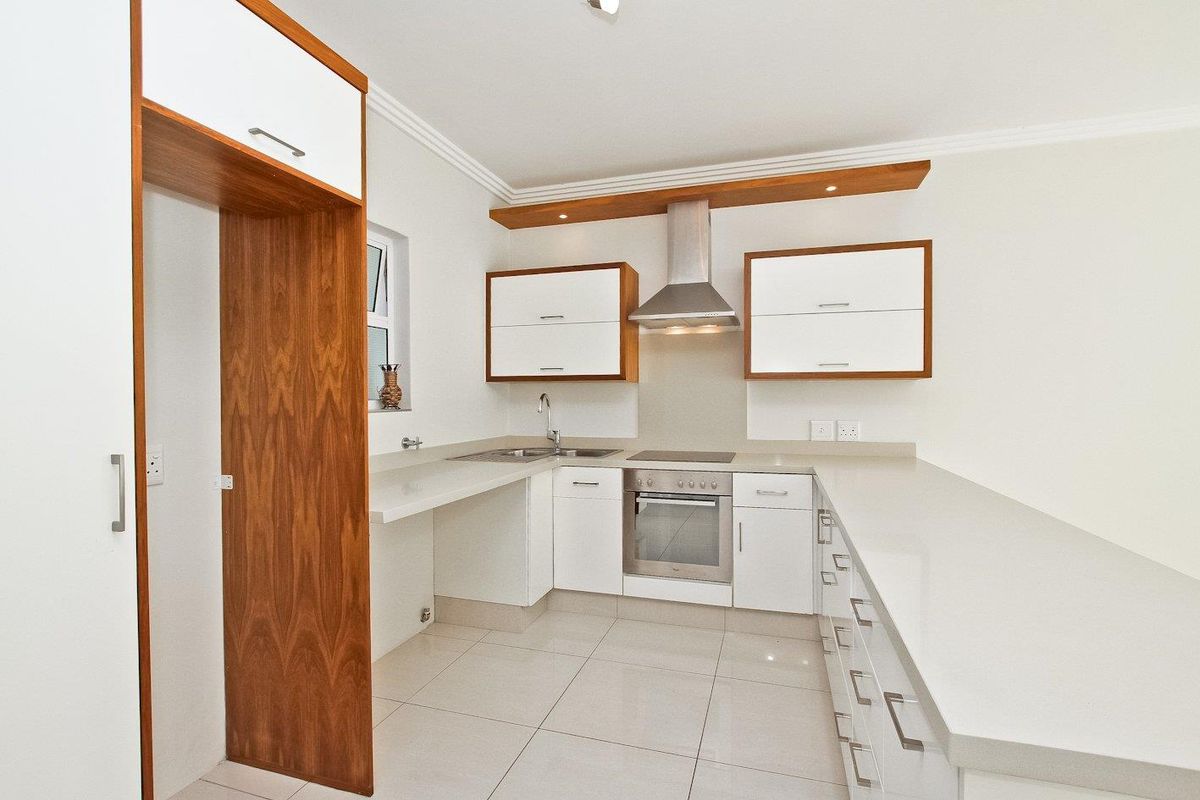 Modern kitchen featuring white cabinetry with wood accents, stone countertops, integrated stainless steel appliances, and tiled flooring.