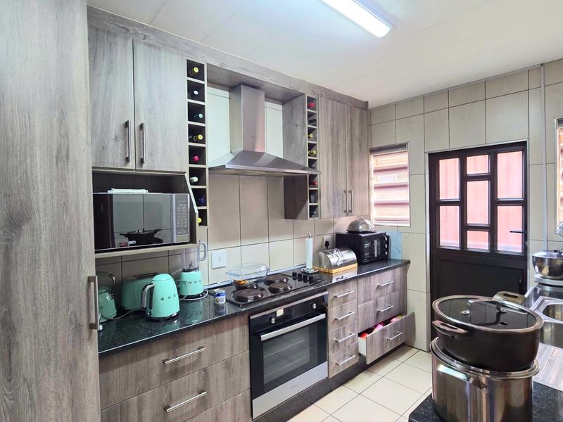 A functional kitchen featuring wood-look cabinetry, granite countertops, a built-in oven with hob, extractor fan, and a double stainless steel sink.