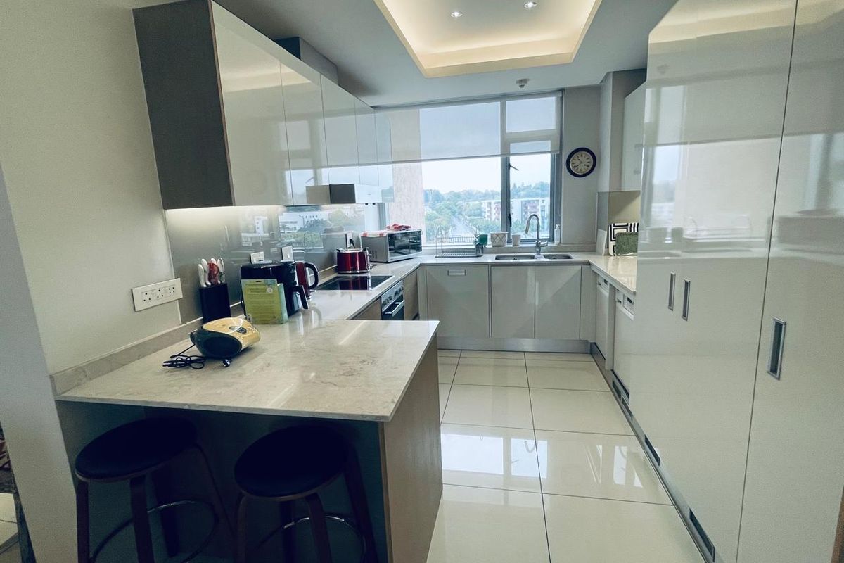 Modern kitchen featuring high-gloss cabinetry, stone countertops, a breakfast bar, integrated appliances, and sleek tiled flooring with ample natural light.