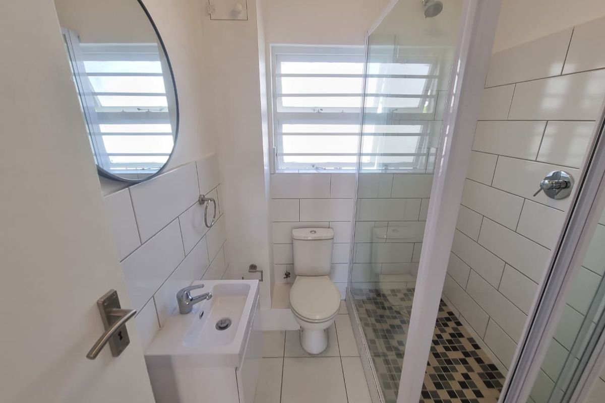 A clean, modern bathroom featuring a vanity basin, toilet, and a glass-enclosed shower with subway wall tiling and mosaic floor accents.