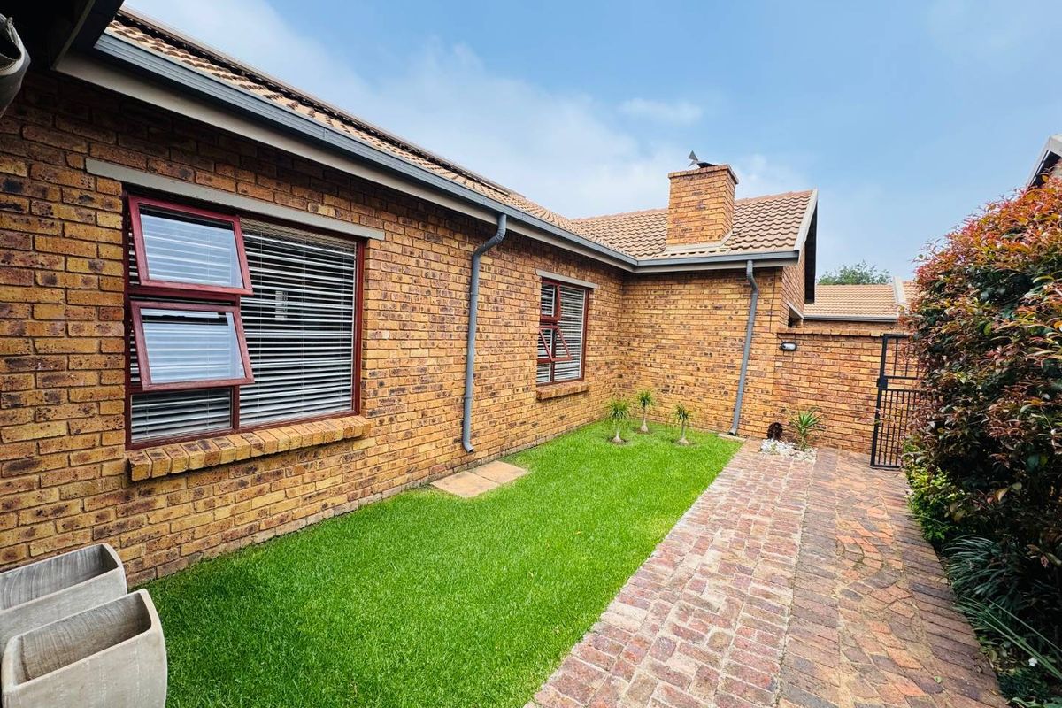 A well-maintained rear exterior view of the townhouse featuring face-brick walls, a tiled roof, a brick-paved pathway, and a neat lawn area.