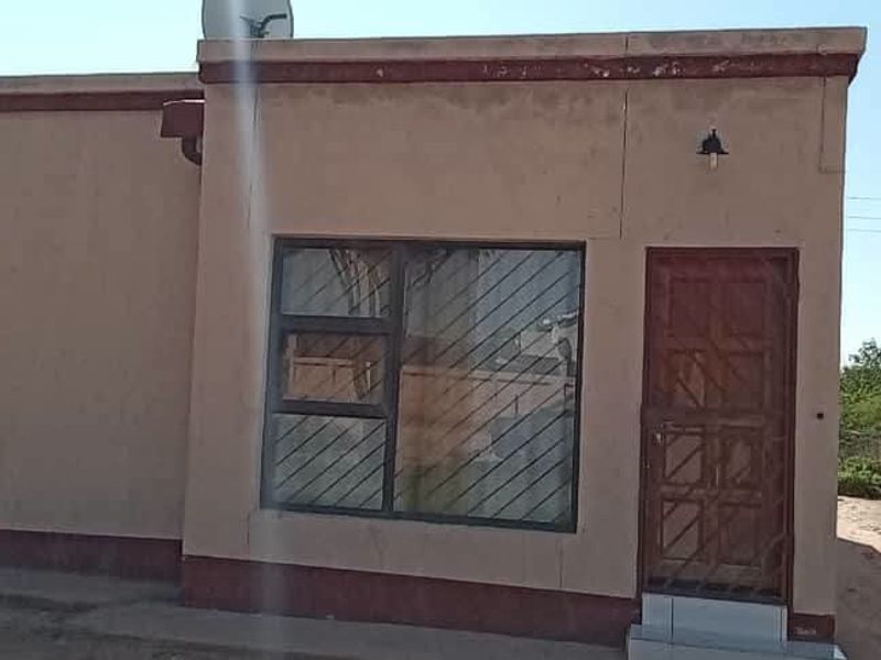 Front elevation of a single-story residential property featuring a security gate, large window, and exterior wall lighting.