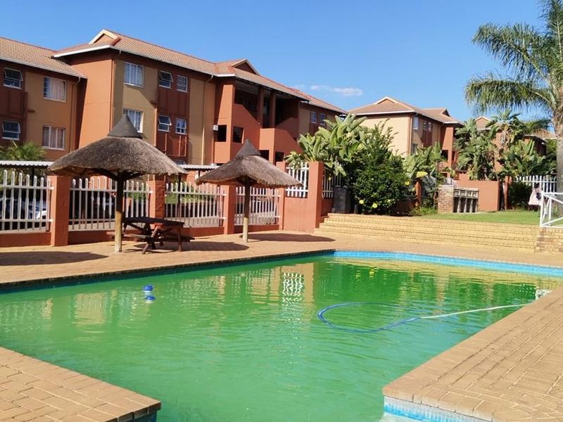 Communal swimming pool area featuring brick paving and thatched umbrellas within an apartment complex setting.