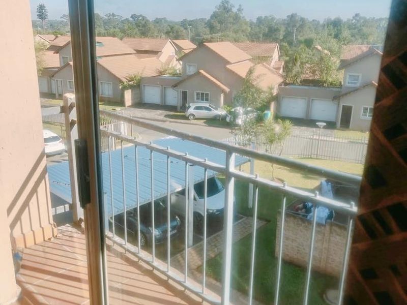 A balcony with tiled flooring and a metal balustrade, offering an elevated view of the surrounding residential complex and parking area.