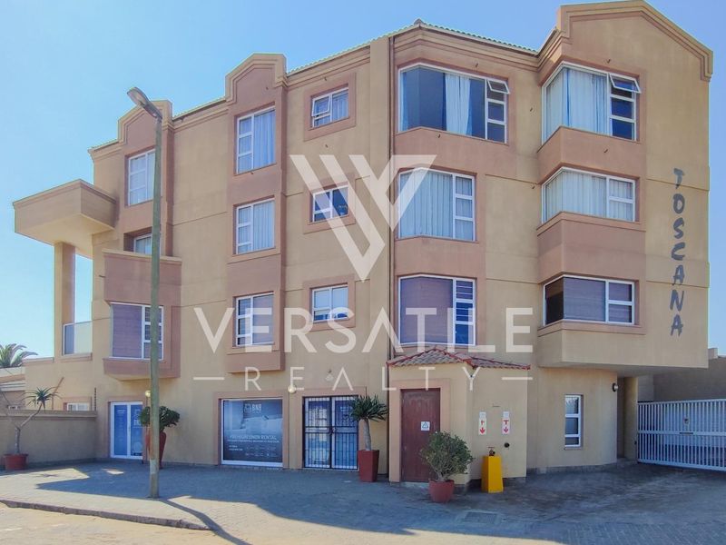 Front elevation of the Toscana apartment complex, featuring a multi-story facade with secure gated access and paved driveway area.