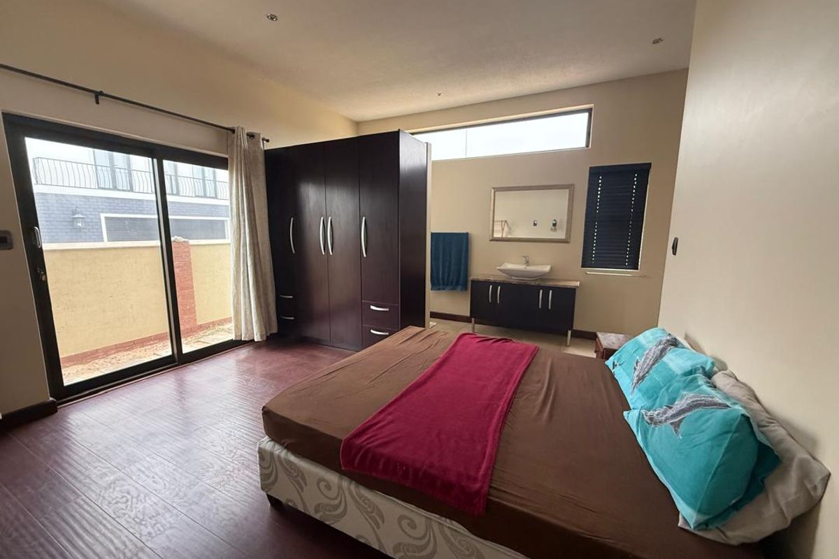 Spacious bedroom featuring dark wood-look flooring, built-in wardrobe, integrated vanity basin, and sliding glass doors leading to an outdoor area.