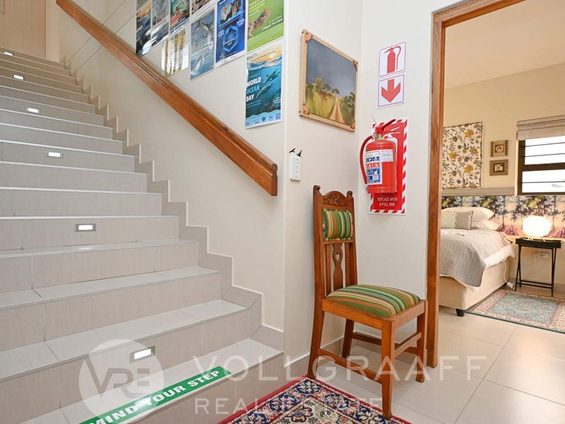 A bright hallway featuring a tiled staircase with integrated lighting, a wooden handrail, and direct access to an adjacent bedroom.