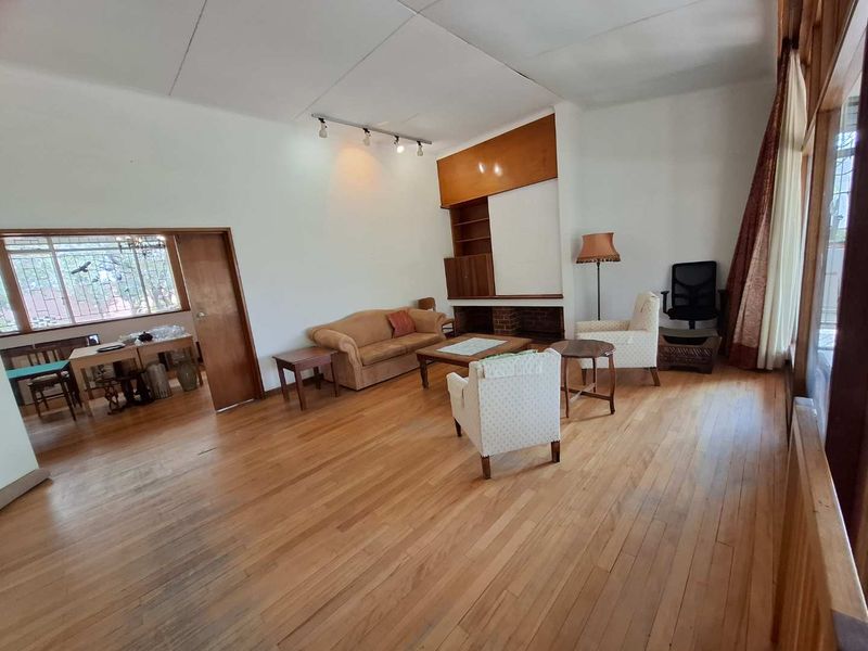 Spacious living room featuring original hardwood flooring, a brick fireplace with built-in shelving, and large windows providing ample natural light.