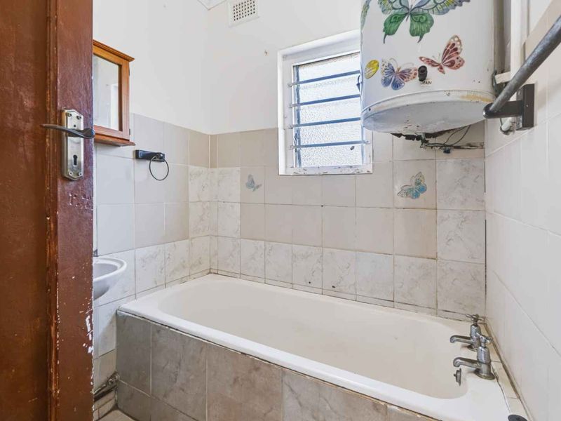 A dated bathroom featuring a bathtub, wall-mounted water heater, and tiled walls, requiring modernization and cosmetic updates to improve its overall condition.