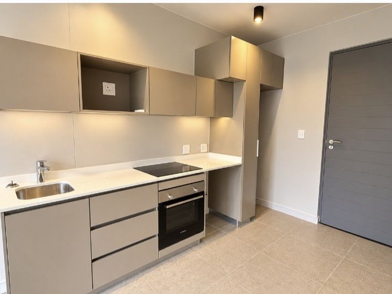 Modern, minimalist kitchen featuring sleek taupe cabinetry, stone countertops, integrated electric hob and oven, and high-quality tiled flooring in a clean, neutral space.