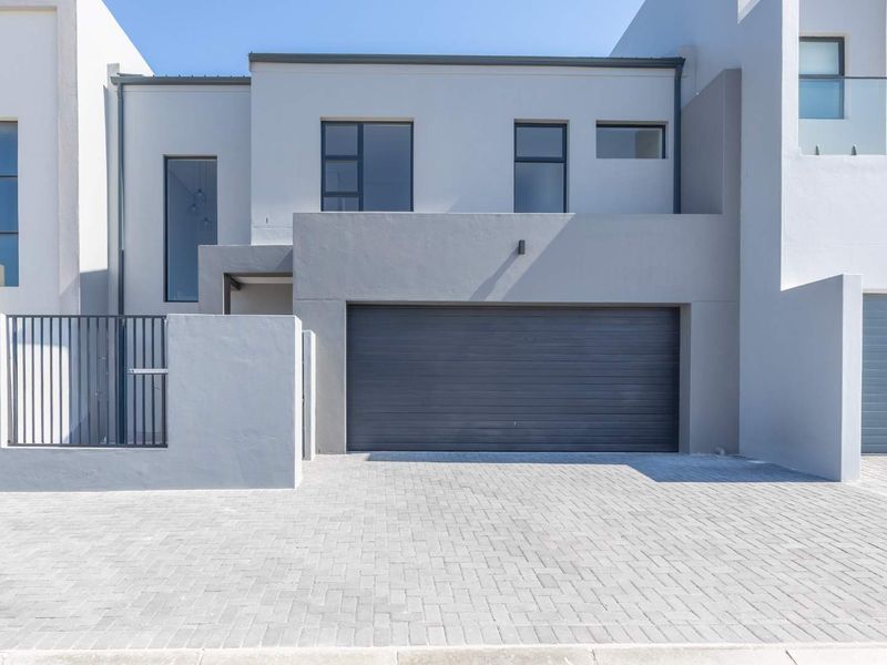 Modern double-storey townhouse facade featuring a paved driveway, secure garage, and clean architectural lines with contemporary grey finishes.
