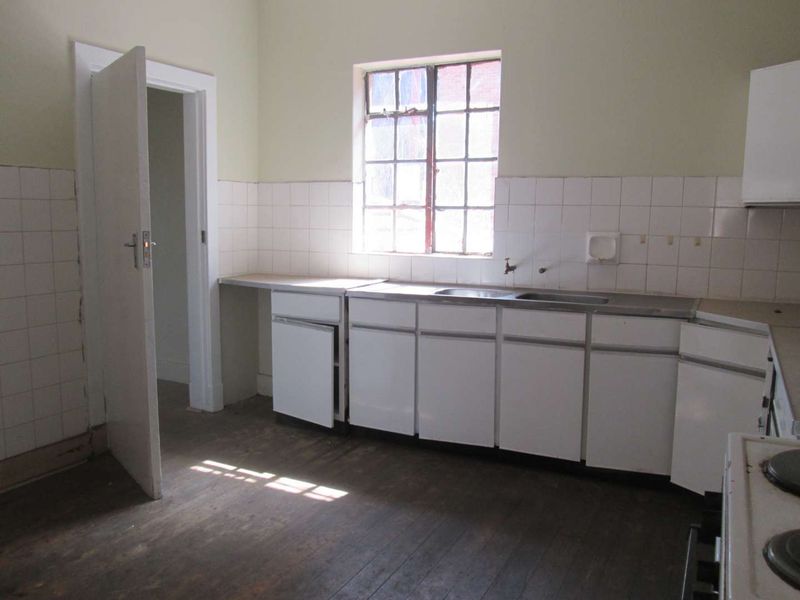 A dated, empty kitchen featuring original timber flooring, white cabinetry, a stainless steel sink, and tiled splashbacks, offering significant potential for renovation.
