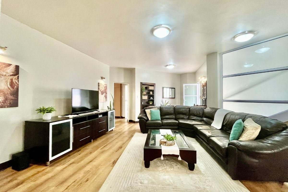 A spacious living room featuring modern wood-look flooring, recessed ceiling lighting, and a large glass partition wall.