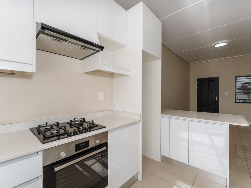 Modern kitchen featuring white cabinetry, stone countertops, a built-in oven with gas hob, extractor fan, and a convenient breakfast bar area.