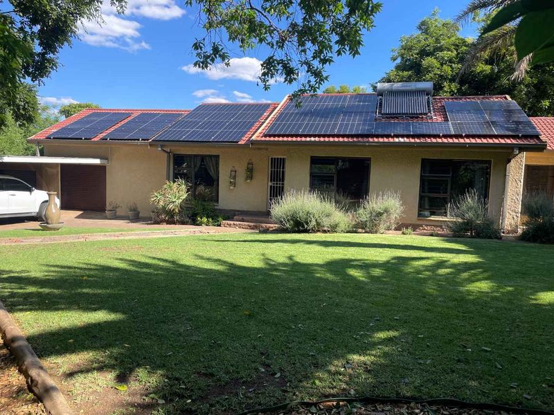 Front view of a single-story house featuring a well-maintained lawn, a tiled roof equipped with solar panels and a solar water heater, and a garage.