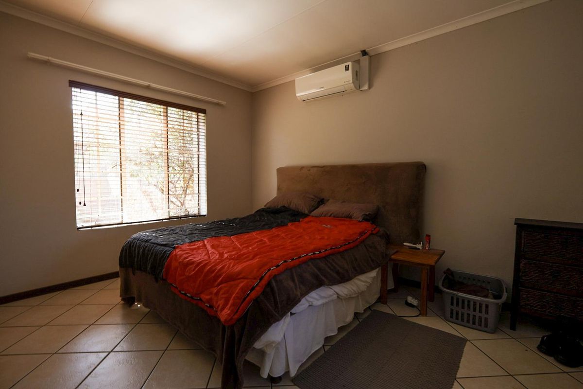 A bedroom featuring tiled flooring, a wall-mounted split-system air conditioner, and venetian blinds on the window.