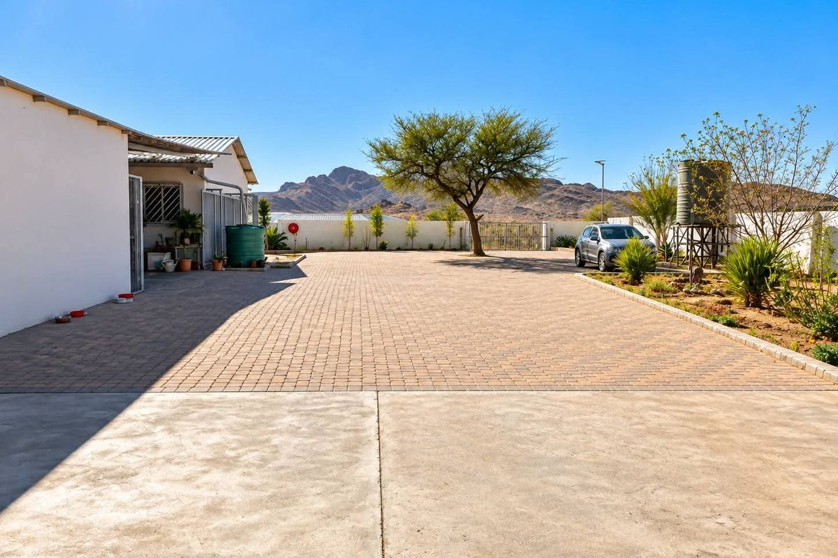 Spacious paved rear courtyard featuring a concrete apron, water storage tank, and perimeter wall with mountain views.