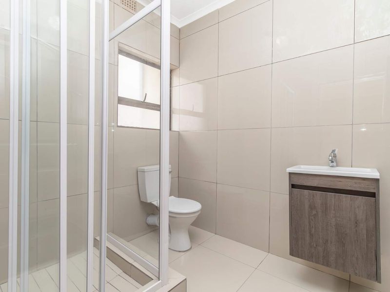 A clean, modern bathroom featuring a glass shower enclosure, a wall-mounted vanity with basin, and neutral floor-to-ceiling wall tiles.