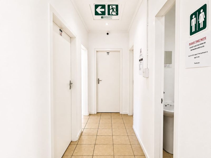 A functional hallway featuring tiled flooring, emergency exit signage, and multiple internal doors leading to various rooms.