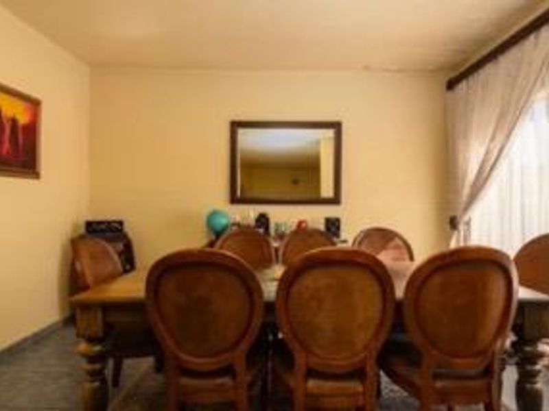 A dining room area featuring neutral wall finishes and a window with curtain rails, showing signs of ceiling water damage.