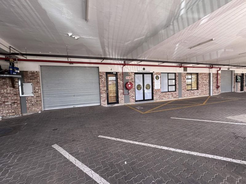 A covered parking area featuring exposed brickwork, roller shutter doors, and functional fire safety equipment, providing secure access to the building.