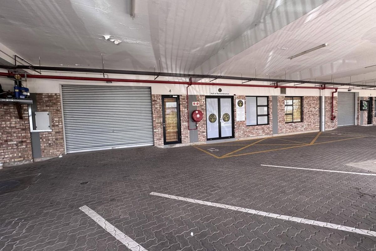 A covered parking area featuring exposed brickwork, roller shutter doors, and functional fire safety equipment, providing secure access to the building.