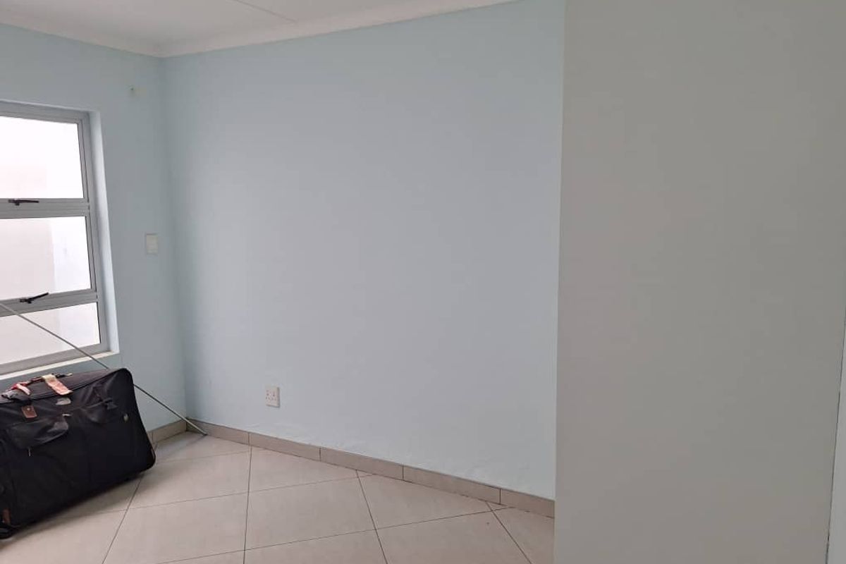 A vacant bedroom featuring neutral light blue walls, tiled flooring, and an aluminium-framed window.