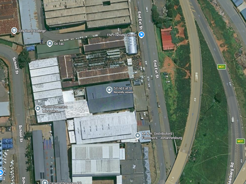 Aerial view of an industrial warehouse complex situated near major road networks and commercial facilities in an urban industrial zone.