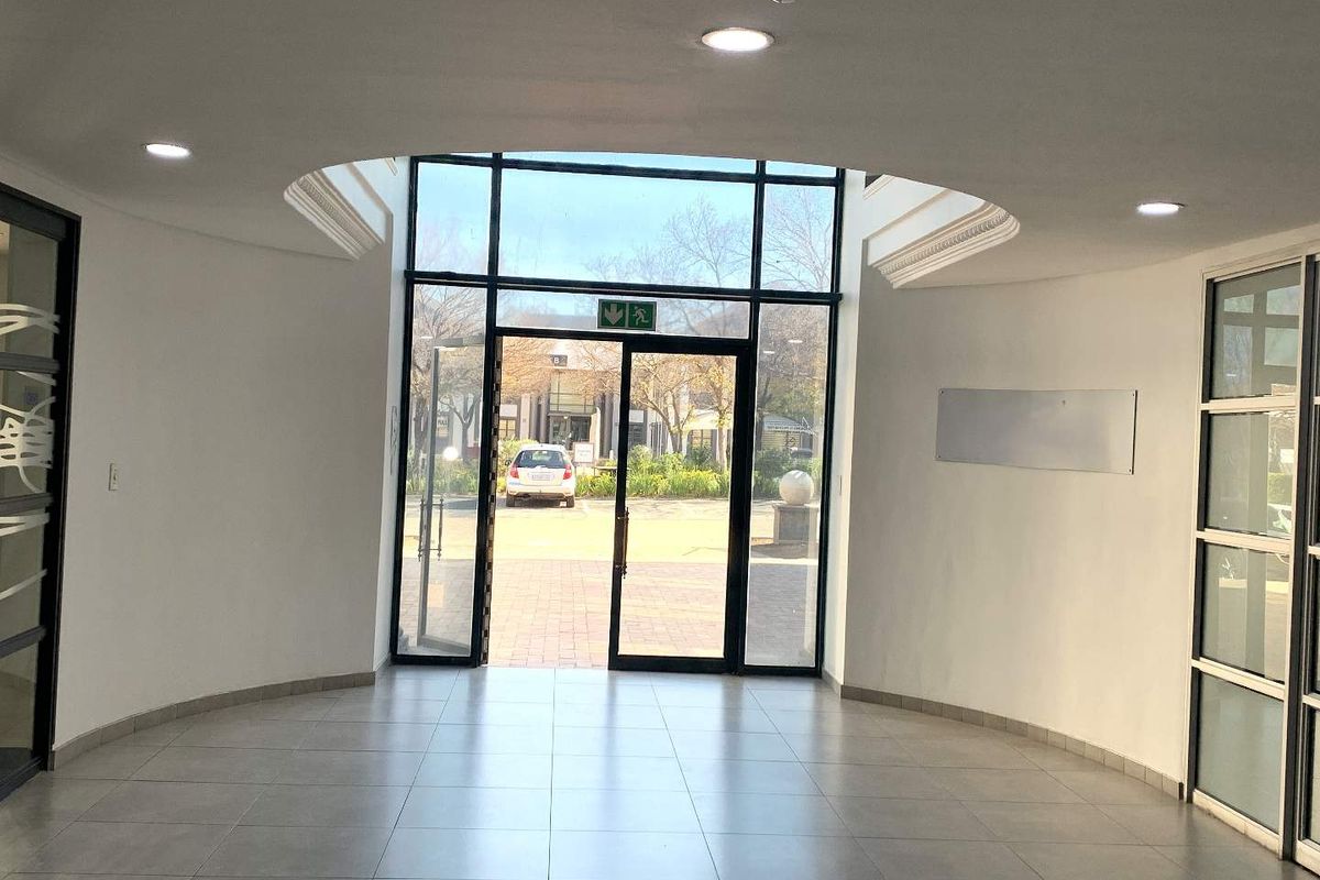 A bright and modern office entrance lobby featuring tiled flooring, recessed ceiling lights, and large glass doors providing natural light and exterior access.