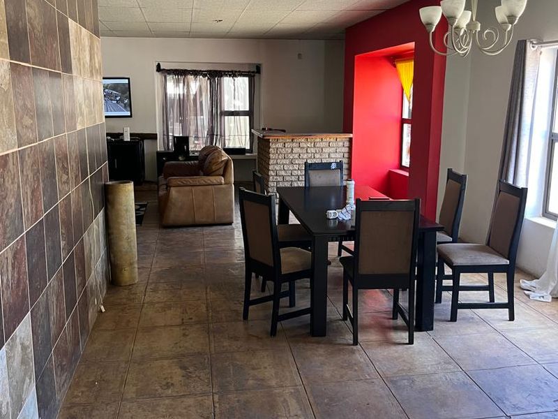 Open plan living and dining area featuring a tiled feature wall, brick fireplace, and drop ceiling tiles with ceramic flooring throughout.