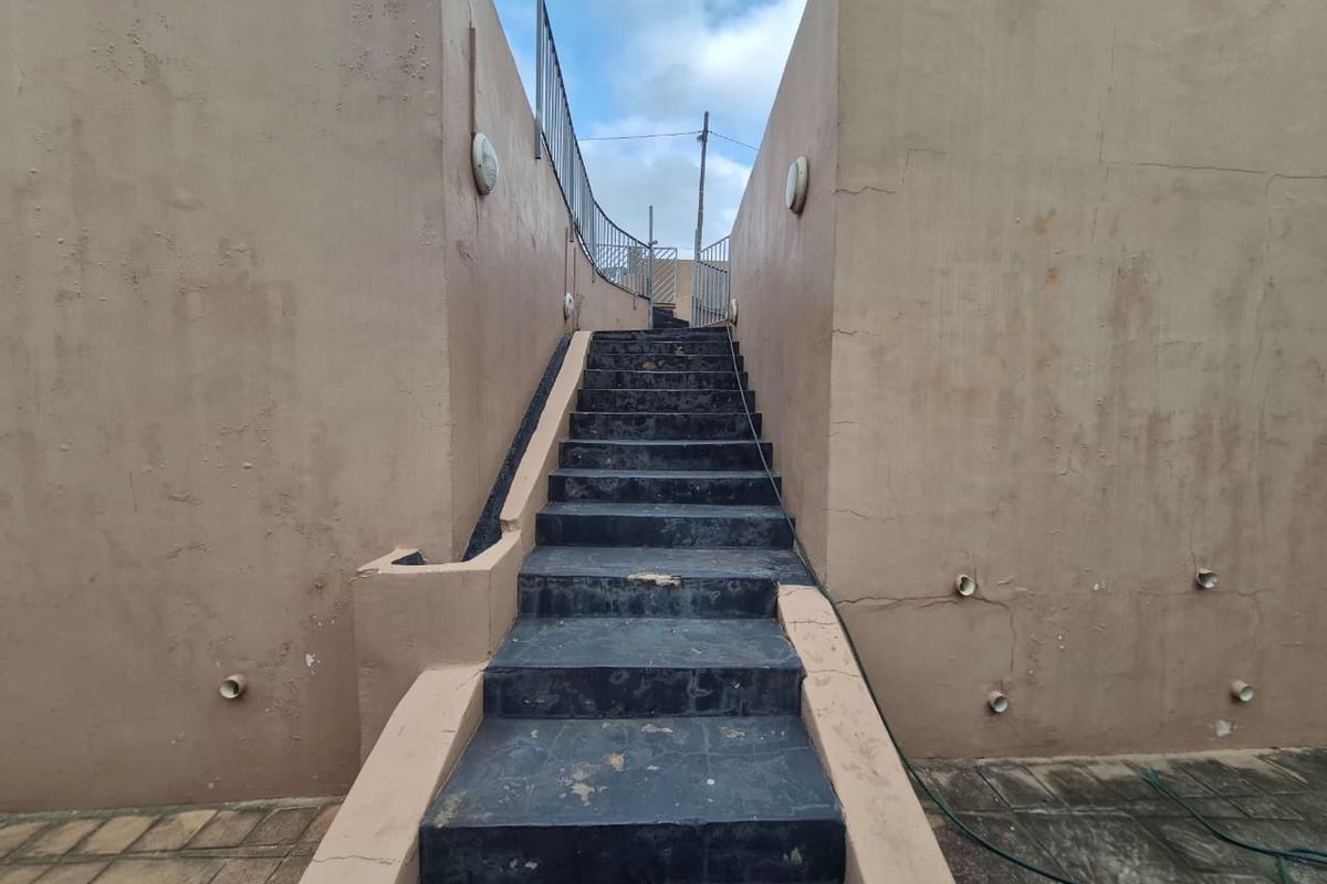 An exterior staircase with metal railings leading upwards, featuring weathered walls and tiled steps showing signs of wear.