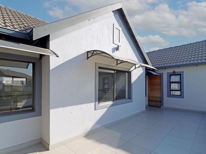 A clean, tiled balcony area featuring modern aluminium window frames, a timber entrance door, and protective awnings over the windows.