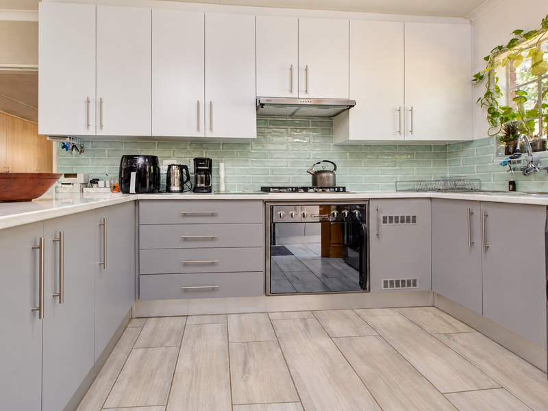 Modern kitchen featuring white upper and grey lower cabinetry, a light green subway tile backsplash, built-in oven, gas hob, and wood-look tile flooring.