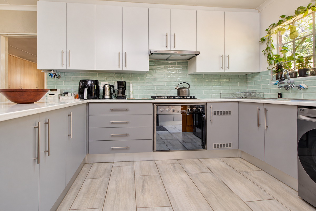 Modern kitchen featuring white upper and grey lower cabinetry, a light green subway tile backsplash, built-in oven, gas hob, and wood-look tile flooring.