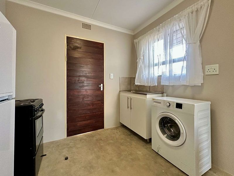 A functional laundry room featuring a built-in sink cabinet, tiled splashback, and a solid timber door.