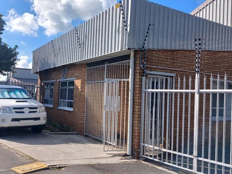 Front exterior view of an industrial property featuring a brick facade, corrugated metal roof, and secure perimeter fencing with an integrated security gate.