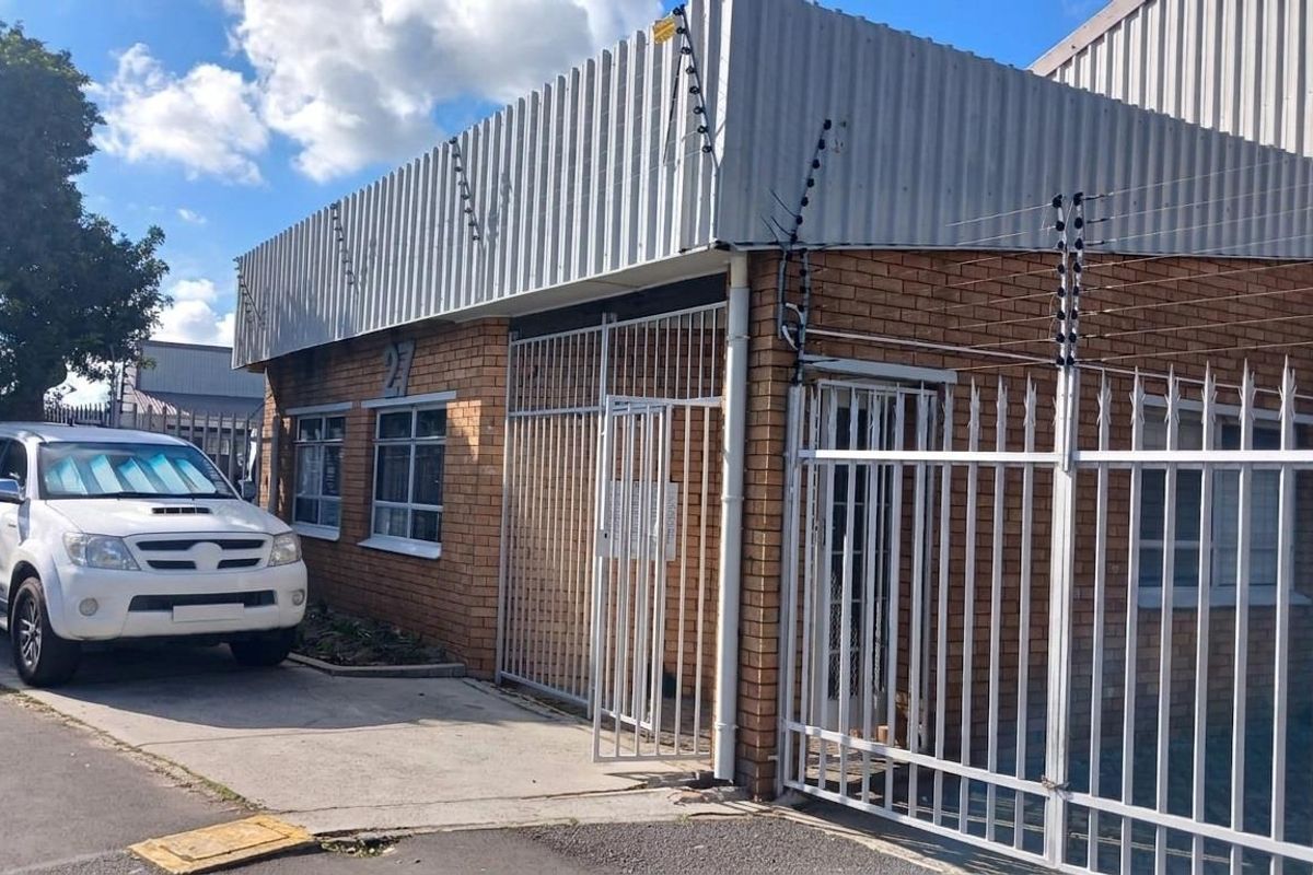 Front exterior view of an industrial property featuring a brick facade, corrugated metal roof, and secure perimeter fencing with an integrated security gate.