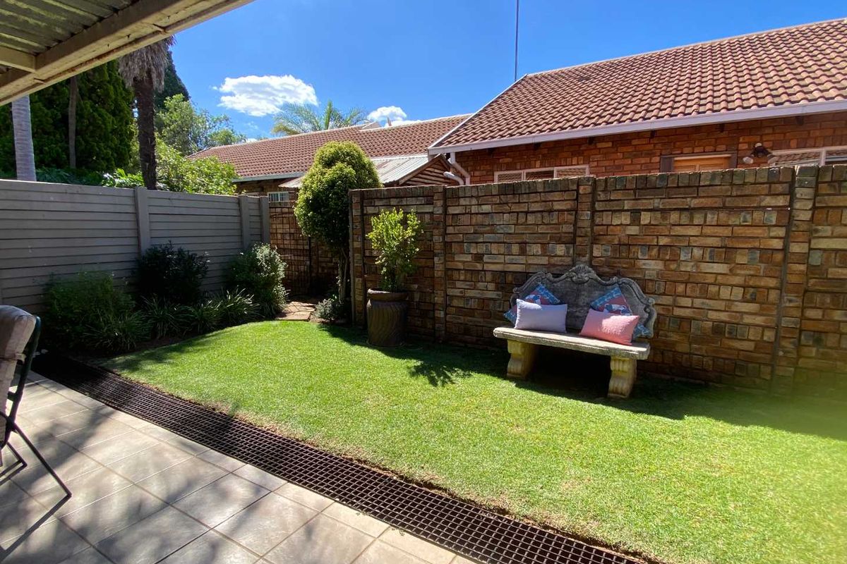 A private rear garden featuring a tiled patio area, a well-maintained lawn, and secure brick boundary walls.