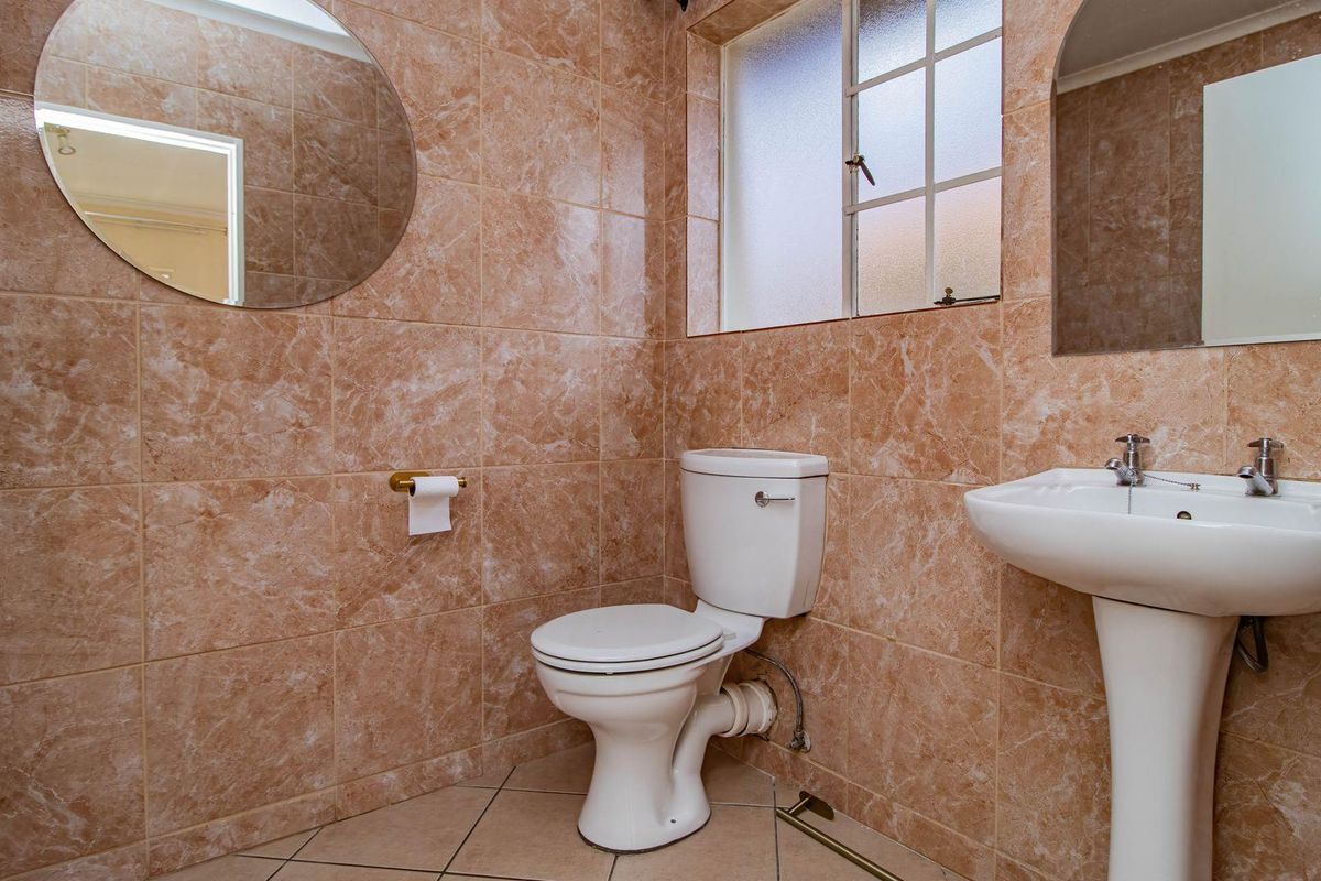 A functional bathroom featuring full-height marble-effect wall tiles, a pedestal basin, and a standard toilet.