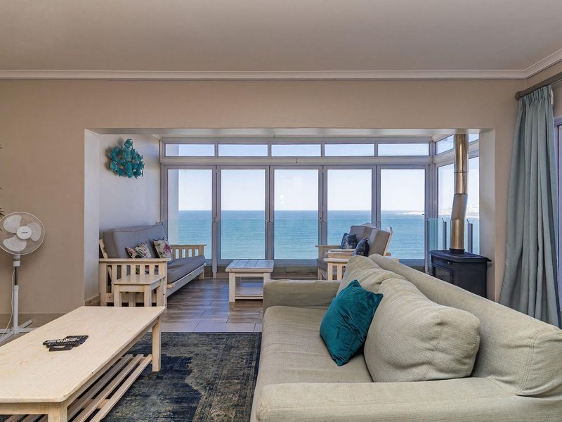 Spacious living room featuring a freestanding fireplace, large sliding glass doors, and expansive ocean views, leading out to a balcony with a glass balustrade.