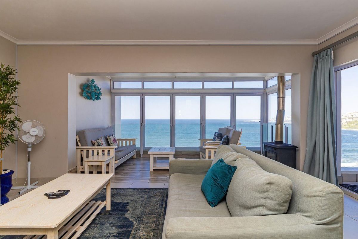 Spacious living room featuring a freestanding fireplace, large sliding glass doors, and expansive ocean views, leading out to a balcony with a glass balustrade.