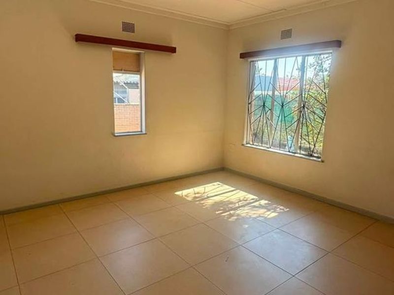 A bright, empty bedroom featuring neutral tiled flooring, security bars on the windows, and simple curtain rails.
