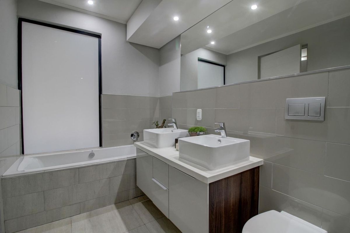 Modern bathroom featuring a double vanity with vessel sinks, a built-in bathtub, large wall mirror, and contemporary tiled finishes.