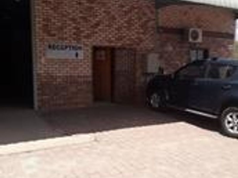 Front exterior view of an industrial property featuring a brick facade, metal roofing, and a paved driveway area.