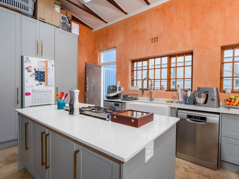 A rustic-style kitchen featuring grey cabinetry, a central island with a gas hob, farmhouse sink, and exposed timber ceiling beams.
