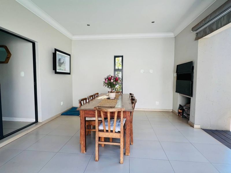 Covered patio area featuring tiled flooring, recessed lighting, and a built-in braai, seamlessly connecting to the garden through large sliding glass doors.