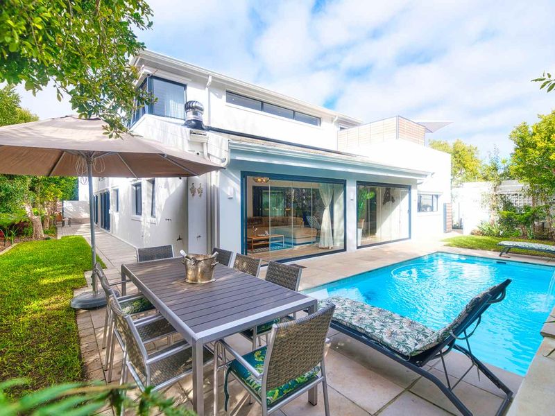 A well-maintained rear exterior featuring a swimming pool, paved patio area, and seamless indoor-outdoor flow through large sliding glass doors.
