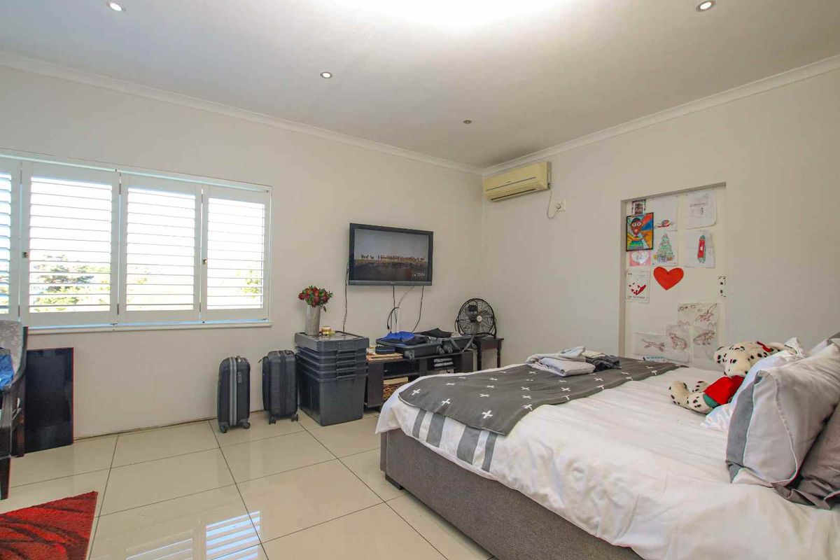 A bedroom featuring tiled flooring, white walls, plantation shutters, and a wall-mounted air conditioning unit.