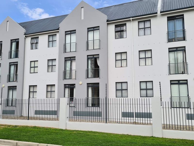 A modern multi-story apartment complex featuring a grey and white facade, metal roof, and secure perimeter fencing with integrated electric security wires.