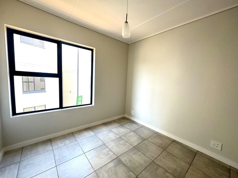 A bright, empty bedroom featuring neutral wall paint, large black aluminium-framed windows, and modern tiled flooring.